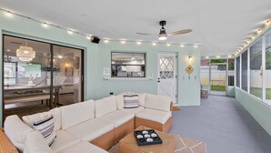 A modern living room with a sectional sofa, a dining table, and a kitchen visible through glass doors.