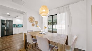 A modern dining area with a wooden table, four chairs, a decorative wall hanging, and a hanging light fixture.