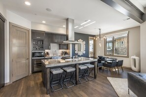 A modern kitchen with dark wood cabinets, a large island with bar stools, and a dining area with a chandelier.