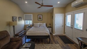 A bedroom with a bed, a ceiling fan, a bedside table, a lamp, a chair, and a window.