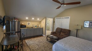 A compact living space with a kitchenette, a ceiling fan, a sofa, a bed, and a dining area.