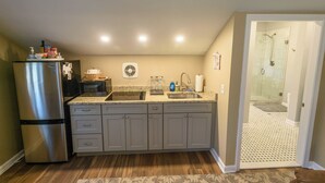 A kitchen with a refrigerator, microwave, sink, and a glass shower door.