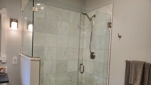 A glass-enclosed shower with a handheld showerhead and a wall-mounted faucet.