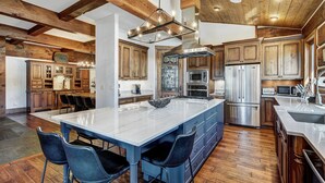 A spacious kitchen with wooden beams, a large island with bar stools, stainless steel appliances, and a rustic tile backsplash.