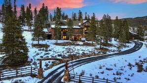 A large, multi-story lodge with a stone facade, surrounded by snow-covered ground and tall pine trees.