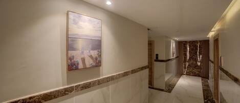 A hallway with marble flooring, a painting on the wall, and a marble wall panel.