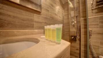 Um banheiro com banheira, box de vidro e três frascos de gel de banho na borda da banheira.