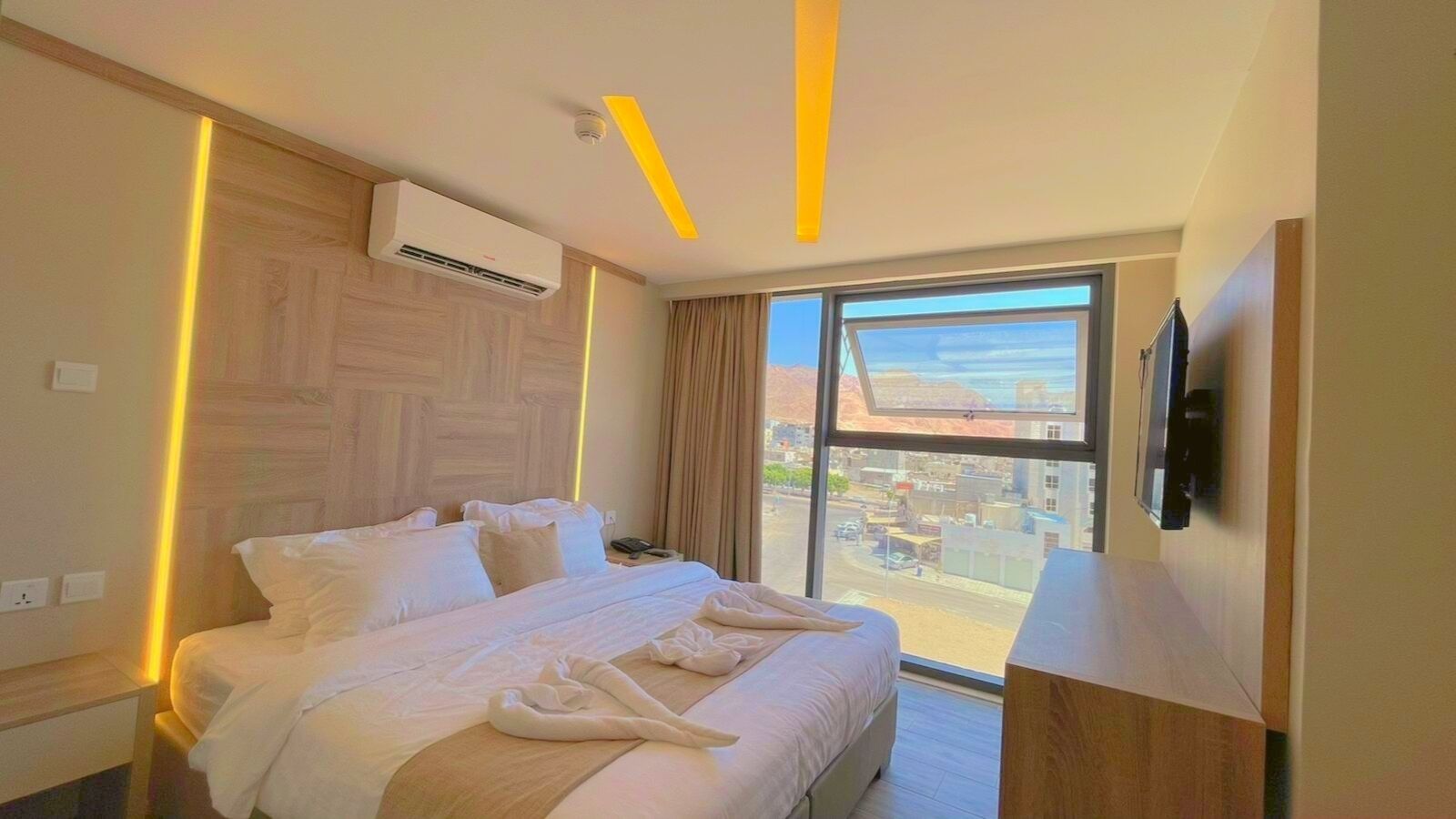 Una camera d'albergo con un letto grande, una TV a schermo piatto montata a parete e una finestra con vista sulla città.