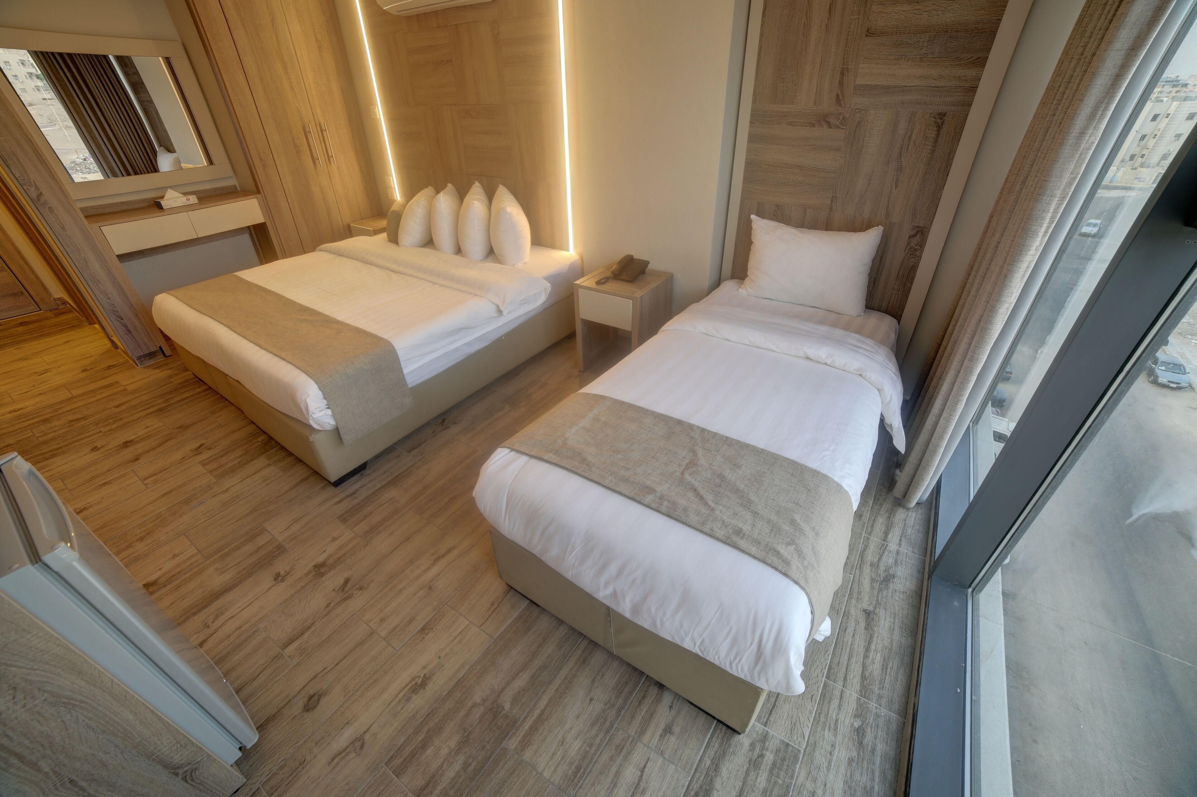Una habitación de hotel moderna con dos camas, una mesita de noche con teléfono, y un ventanal con vistas a la ciudad.
