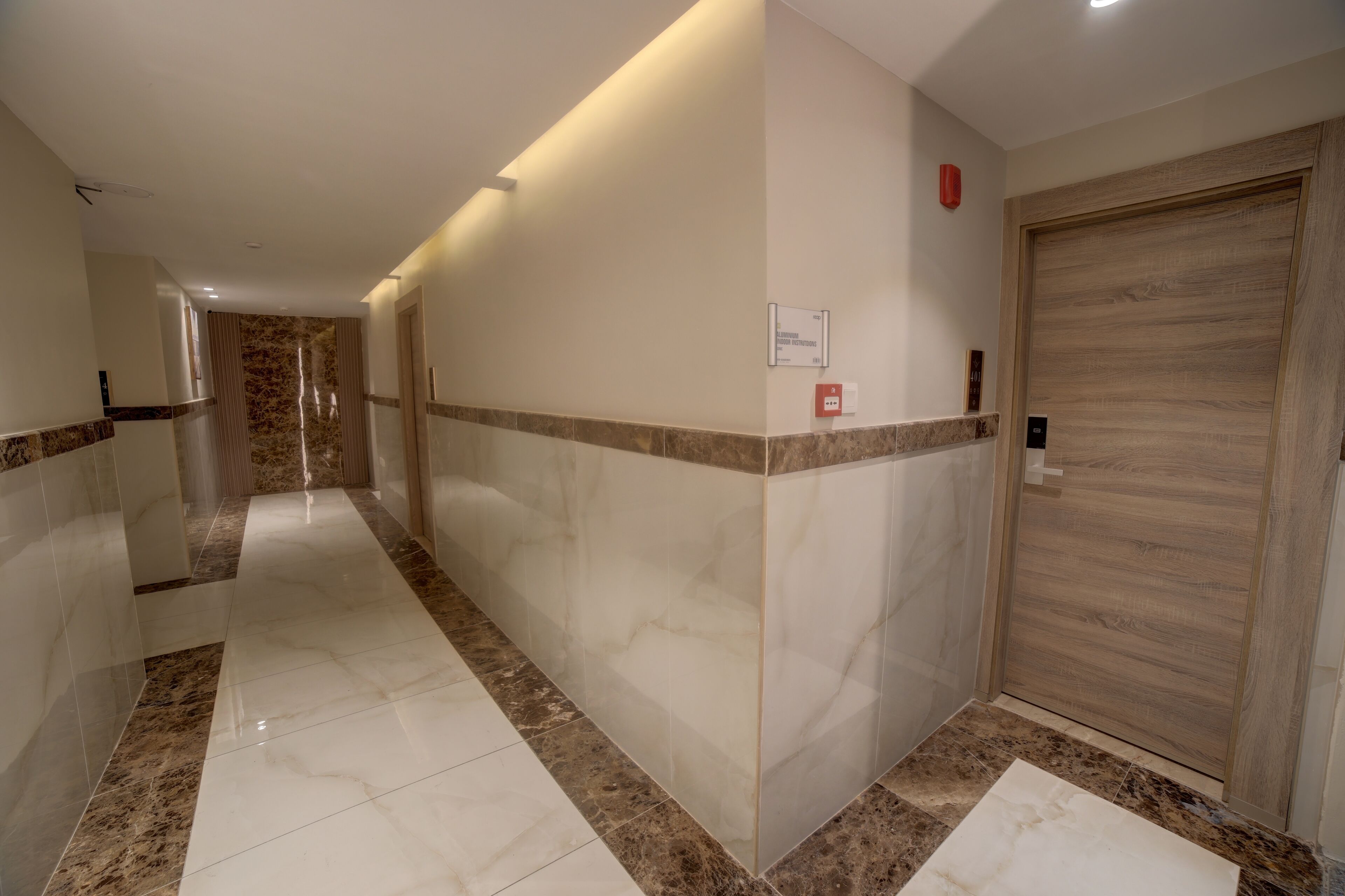 Un pasillo con suelo de mármol, puertas de madera y un detector de incendios en la pared.
