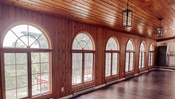 Una habitación espaciosa con paneles de madera, ventanas arqueadas grandes y suelo de madera.