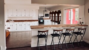 Una cocina moderna con armarios blancos, encimera de madera y una zona de bar con cuatro sillas.