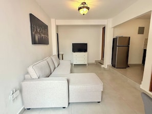 A modern living room with a sectional sofa, a flat-screen TV, and a refrigerator.