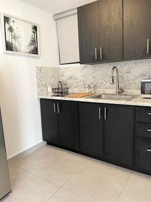 A modern kitchen with dark cabinets, a marble countertop, and a stainless steel sink.