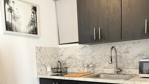 A modern kitchen with dark cabinets, a marble countertop, and a stainless steel sink. - CS4- Impressive Colonial 1BR Apartment w/Private Parking & Open Spaces (San Juan)