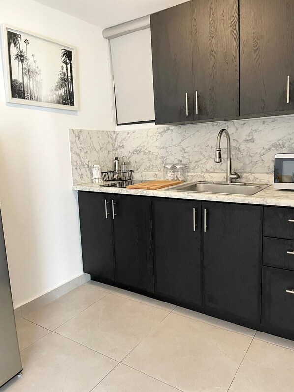 A modern kitchen with dark cabinets, a marble countertop, and a stainless steel sink.