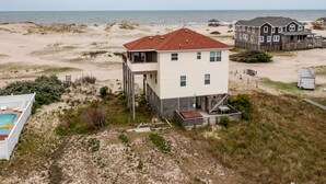 Ein zweistöckiges Strandhaus mit rotem Dach, Pool und Blick auf den Strand.