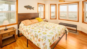 Ein Schlafzimmer mit einem Bett, einem hölzernen Kopfteil, einer Bank und großen Fenstern.