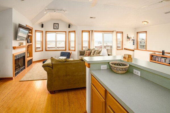 A spacious living area with a fireplace, a sofa, and a kitchen counter with a basket. - Corolla 4x4 beach cottage with phenomenal ocean views! (Corolla)
