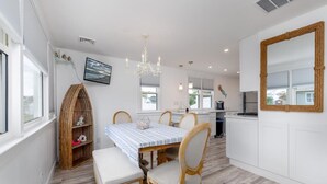 Une cuisine moderne avec des meubles blancs, une table à manger avec des chaises, un banc en bois et un grand miroir au mur.