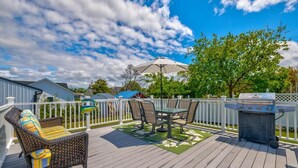 Une terrasse en bois avec des meubles d’extérieur, un barbecue et une clôture blanche.