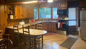 Una cocina de estilo cabaña con zona de comedor, armarios de madera, microondas, estufa y refrigerador.