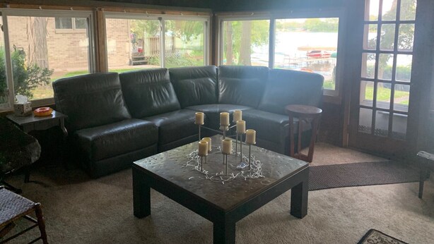 Una sala de estar con un sofá seccional de cuero negro, una mesa de centro con velas y ventanas amplias que ofrecen vistas al exterior.