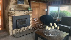 Una sala de estar acogedora con chimenea de ladrillo, puerta de madera, un sillón negro, sofá negro y una mesa con velas.
