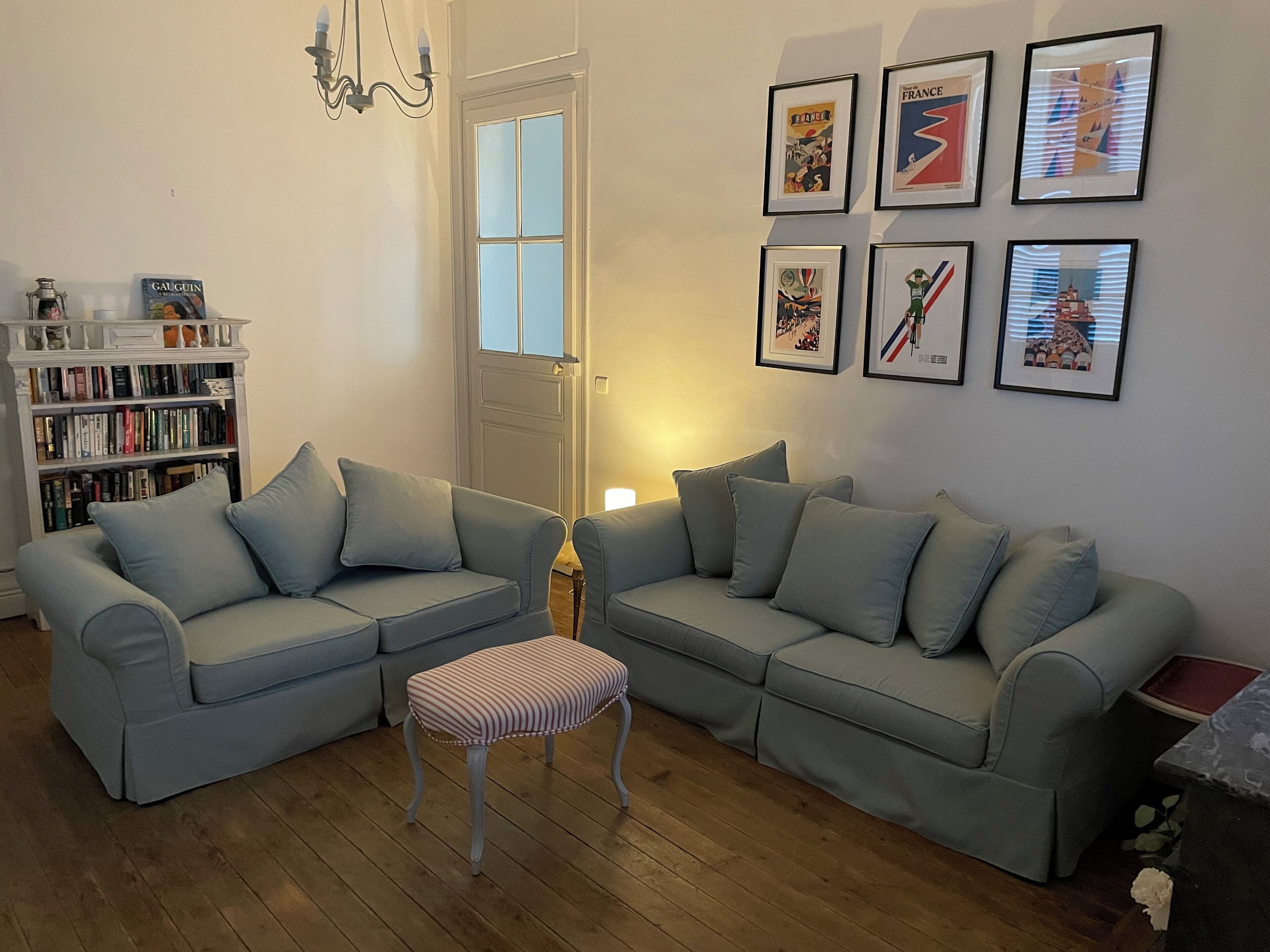 Una sala de estar con dos sofás grises, un reposapiés a rayas, una estantería y una puerta con paneles de vidrio.