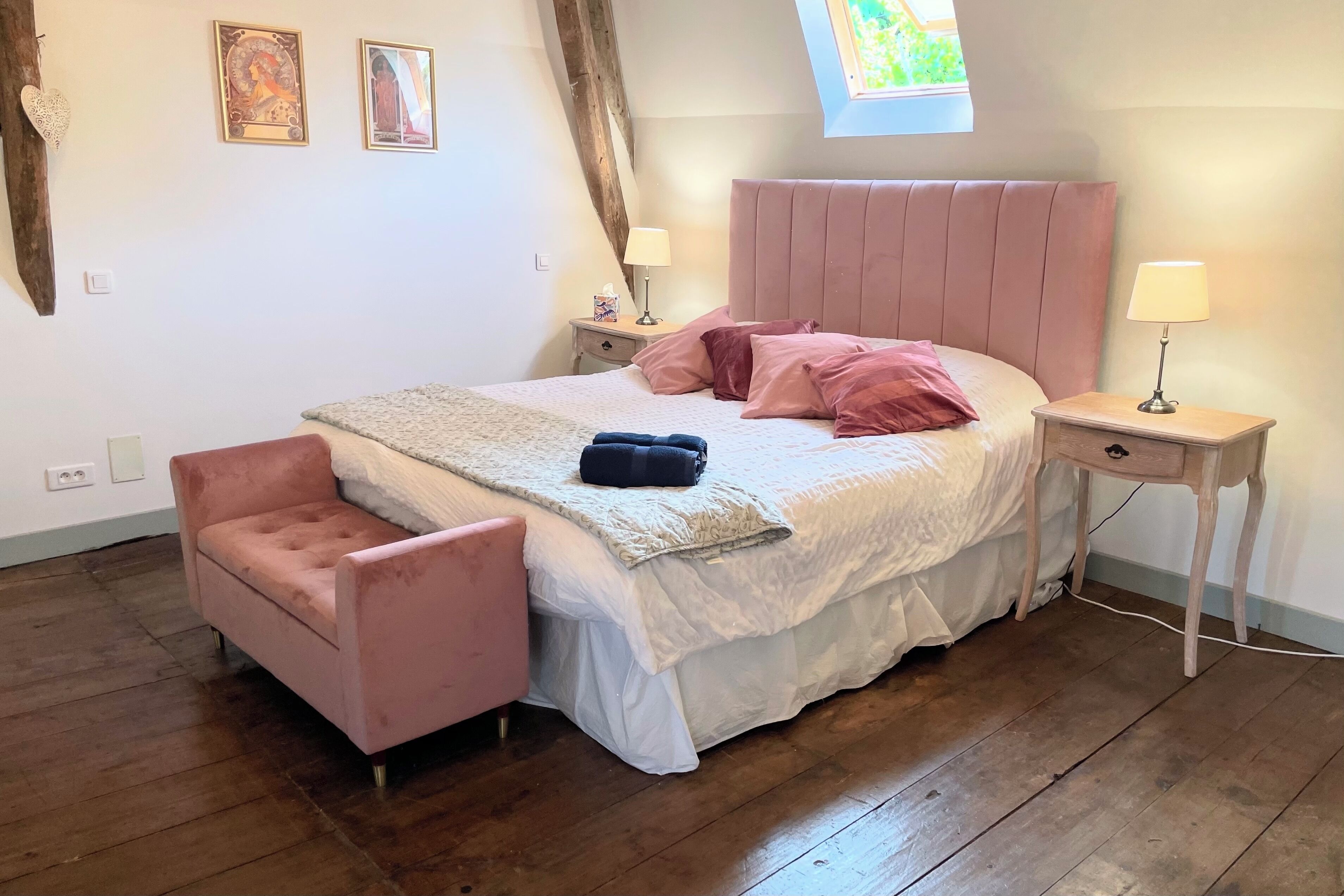Un dormitorio con una cama, una silla rosa, una mesita de noche y una ventana.