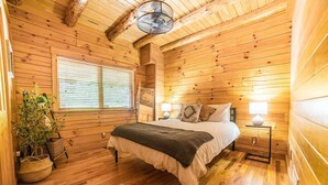 Un dormitorio de cabaña de madera acogedor, con cama, lámparas de noche, una ventana con persianas y una planta en maceta.