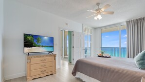 A bedroom with a TV, wooden dresser, bed, and a balcony with a view of the ocean. - Spacious Corner Unit! Oceanfront! Majestic! Pools! (Panama City Beach)