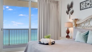 A hotel room with a large balcony, a bed with a neatly made bed, a lamp, and a decorative wall piece. - Spacious Corner Unit! Oceanfront! Majestic! Pools! (Panama City Beach)