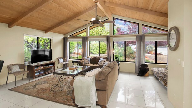 A spacious living room with a high ceiling, large windows, a ceiling fan, a flat-screen TV, a sofa, a coffee table, and a patterned rug. - Red Rock Retreat • Golf • Hiking & Biking Trails • Views • Dining VOC •Adventure (Sedona)