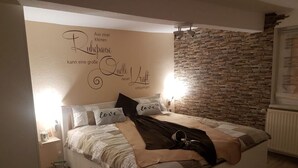 A bedroom with a stone wall, a bed with a headboard that has a decorative wall decal, and a bedside table with a lamp. - Vacation apartment "Haus Herzblick" directly on the pilgrimage path "Herzweg des Friedens" in Ts. (Berghausen)