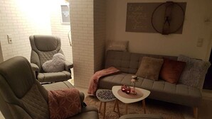 A living room with a grey sofa, two armchairs, a small round coffee table, and a decorative wall clock. - Vacation apartment "Haus Herzblick" directly on the pilgrimage path "Herzweg des Friedens" in Ts. (Berghausen)