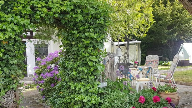 A garden with a pergola covered in ivy, a table with chairs, and various potted plants. - Vacation apartment "Haus Herzblick" directly on the pilgrimage path "Herzweg des Friedens" in Ts. (Berghausen)
