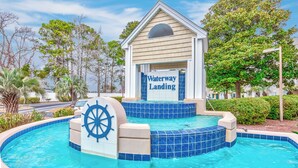 A pool area with a 'Waterway Landing' sign, surrounded by palm trees and a clear sky.