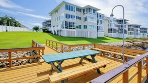 A multi-story building with a white exterior and large windows, a wooden deck with benches, and a clear sky.