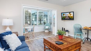 A living room with a blue sofa, a wooden coffee table, a television, and a dining area with a table and chairs.