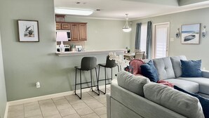Un salon moderne avec un canapé gris, un petit coin cuisine doté de meubles en bois et une table à manger avec des chaises.