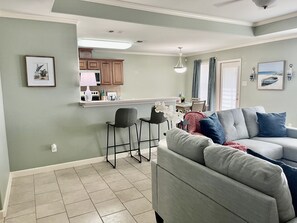 Cozy living space with a kitchen, dining, and seating area, featuring a sofa, table, chairs, and framed pictures.
