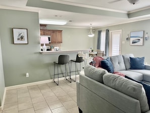 Cozy living space with a kitchen, dining, and seating area, featuring a sofa, table, chairs, and framed pictures.