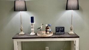 Une console blanche, ornée de deux lampes, d’un oiseau décoratif, d’un panneau et d’un vase.