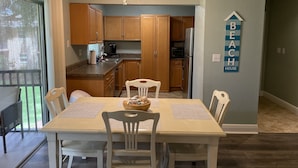 A kitchen with wooden cabinets, a refrigerator, and a ceiling fan. There is a dining table with chairs and a sign on the wall that says "BEACH HOUSE". - Cute, spacious 2 BR 2 Full BA condo minutes from the beaches (Largo)