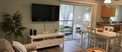 A living room with a sofa, a coffee table, a TV, and a dining area with chairs and a table.
