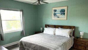 A bedroom with a bed, wooden nightstands, a ceiling fan, a window with curtains, and a framed picture on the wall. - Cute, spacious 2 BR 2 Full BA condo minutes from the beaches (Largo)