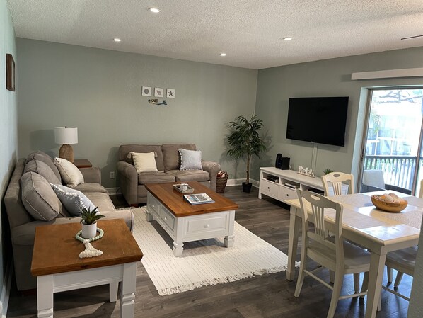 A living room with a sofa, coffee table, TV, and dining area. - Cute, spacious 2 BR 2 Full BA condo minutes from the beaches (Largo)