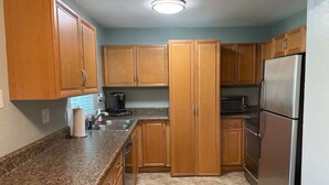 A compact kitchen with wooden cabinets, a granite countertop, a stainless steel refrigerator, and a microwave. - Cute, spacious 2 BR 2 Full BA condo minutes from the beaches (Largo)