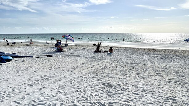 A beach with people swimming and sunbathing, a colorful umbrella, and footprints in the sand. - Cute, spacious 2 BR 2 Full BA condo minutes from the beaches (Largo)